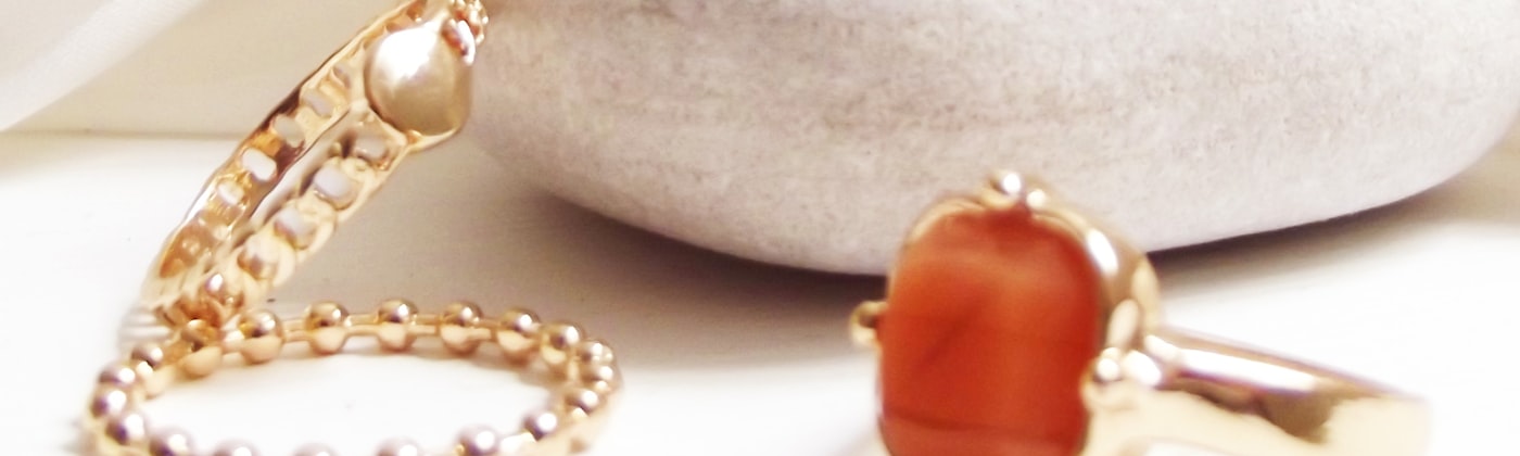 Gold and gemstone rings styled on a neutral surface for a premium jewellery e-commerce website